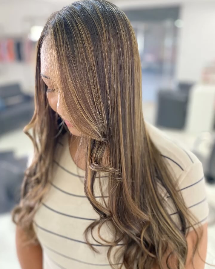 Cabelo castanho longo com mechas iluminadas e pontas onduladas, de perfil
