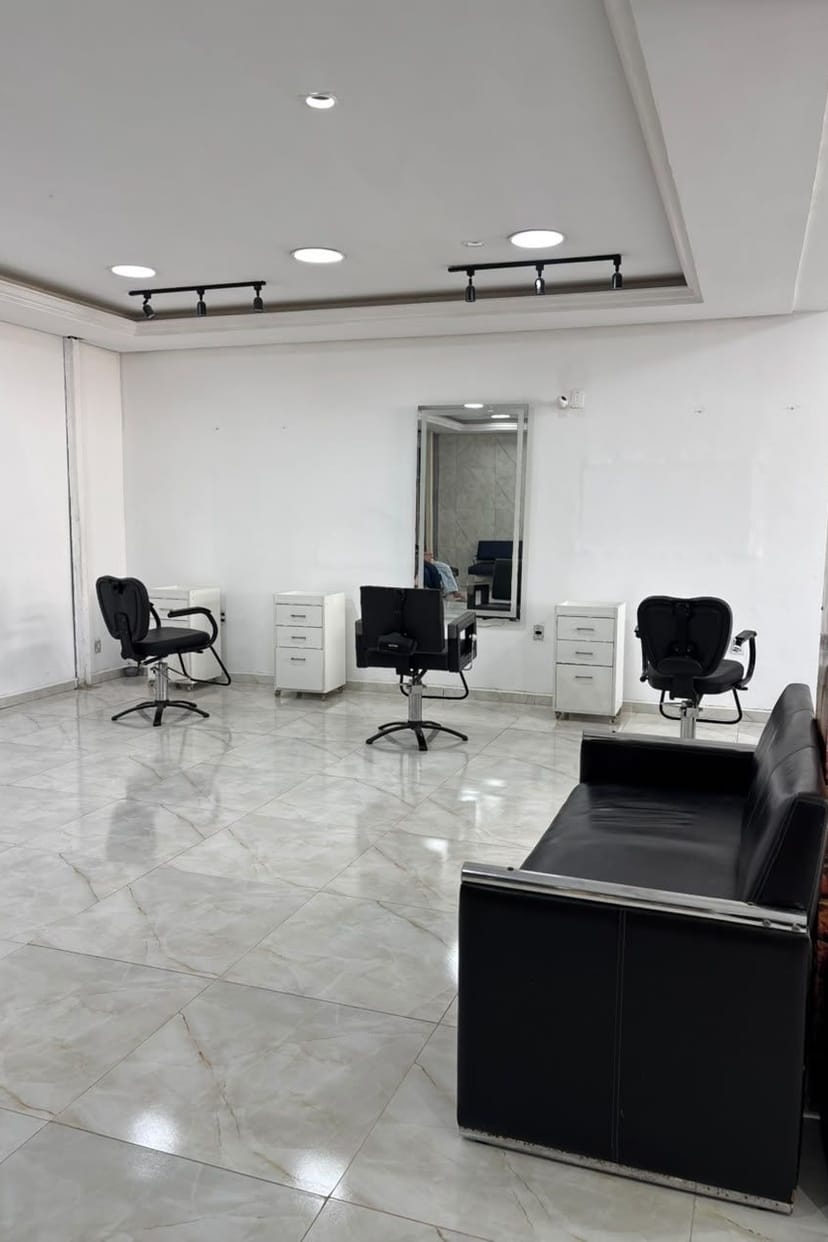 Interior do salão, com cadeiras pretas, espelho e piso de porcelanato claro