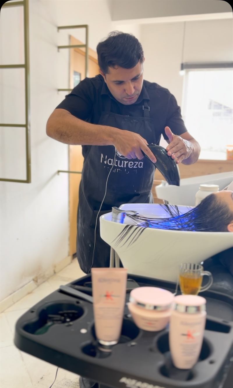 Roberto, dono do salão, concentrado aplicando tratamento no cabelo de uma cliente no lavatório